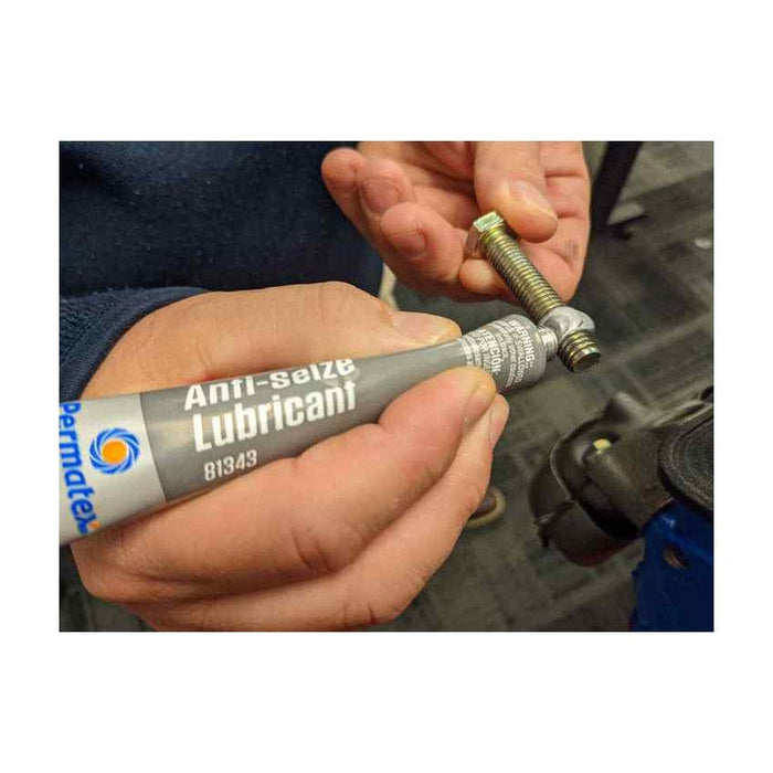Hands holding a bolt and applying permatex anti seize lubricant